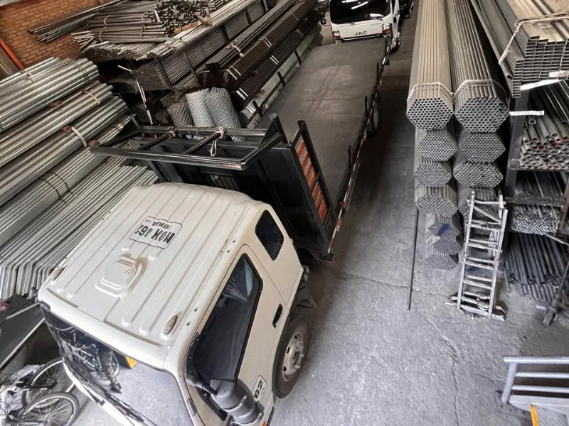 Interior de bodega con atados de tubería y un camión de carga